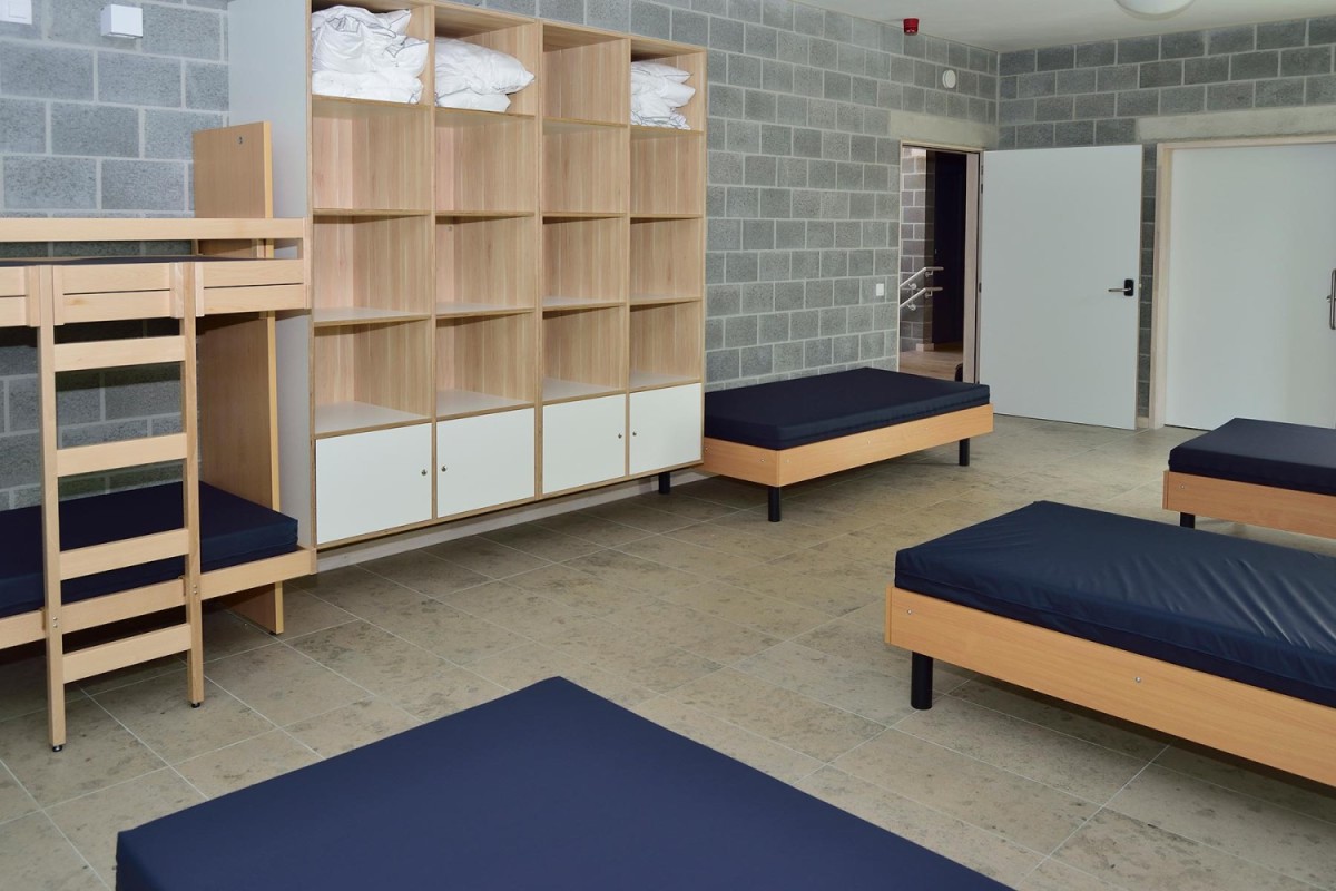Een kamer met stapelbedden en twee eenpersoonsbedden, witte kasten en grijze stenen muren.